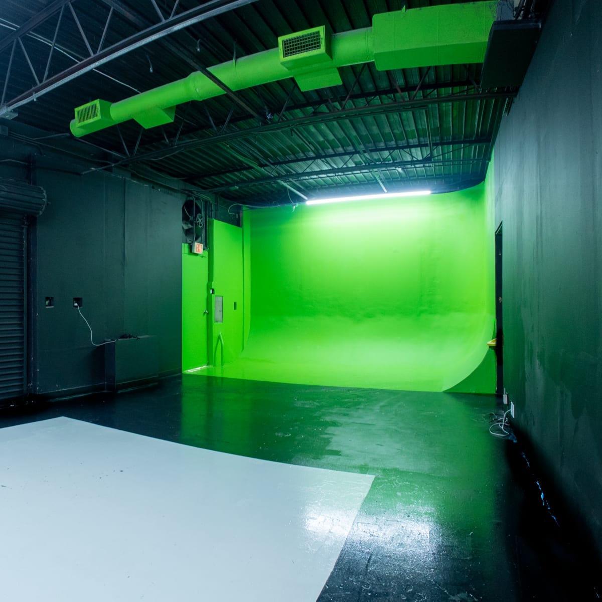 A photography studio with a white backdrop on one side and a bright green backdrop on the other, along with a rolling shutter door and overhead lighting.