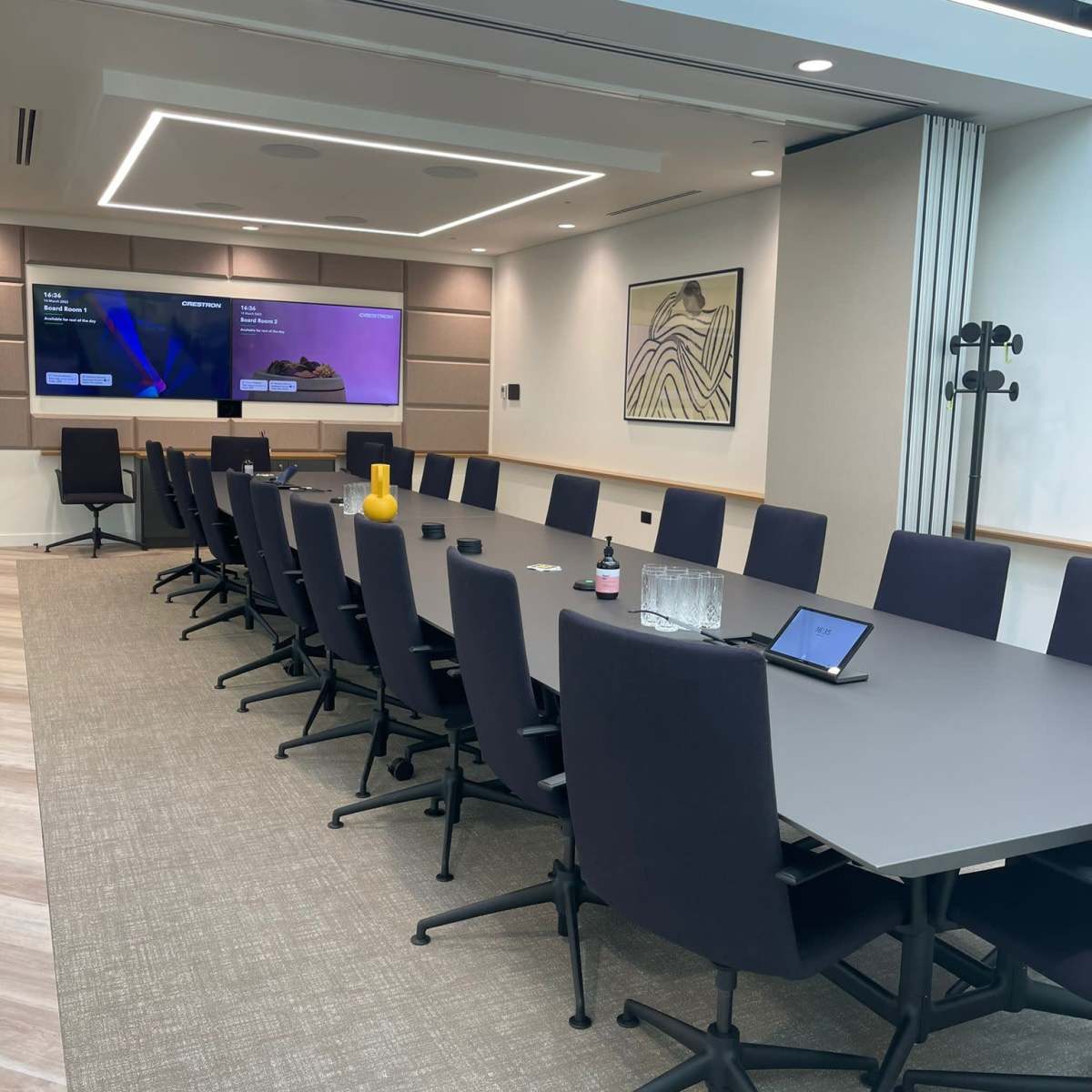 A modern conference room with a long table, black chairs, a large screen, and minimal decorative elements.