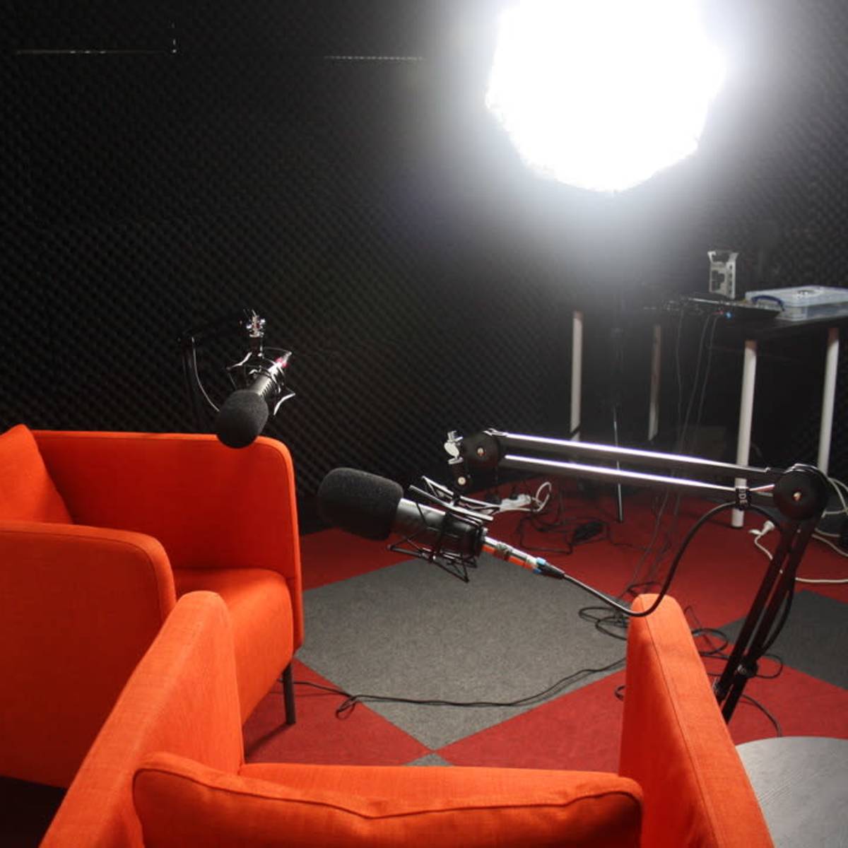 Two orange chairs facing each other under bright lighting in a soundproof studio with black acoustic panels.