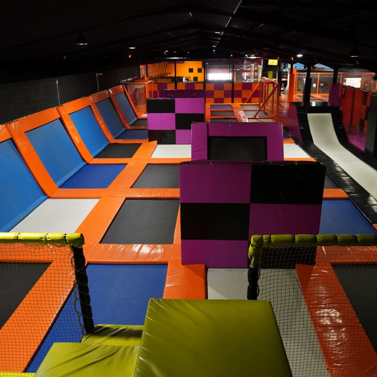 An indoor trampoline park featuring multiple trampolines, foam pits, and colorful safety pads arranged throughout the space.