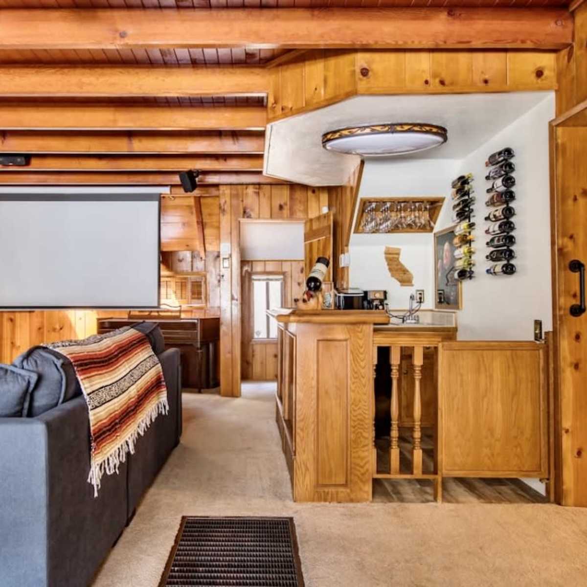 The room features wooden paneling, a sectional couch, a beverage bar, and a projector screen mounted on the wall.