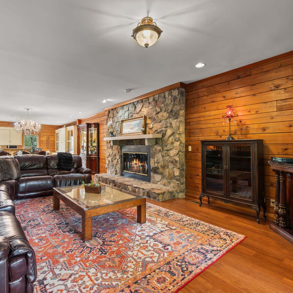 The living room features a leather sectional sofa, a stone fireplace, and wooden walls, with a large area rug on the hardwood floor.