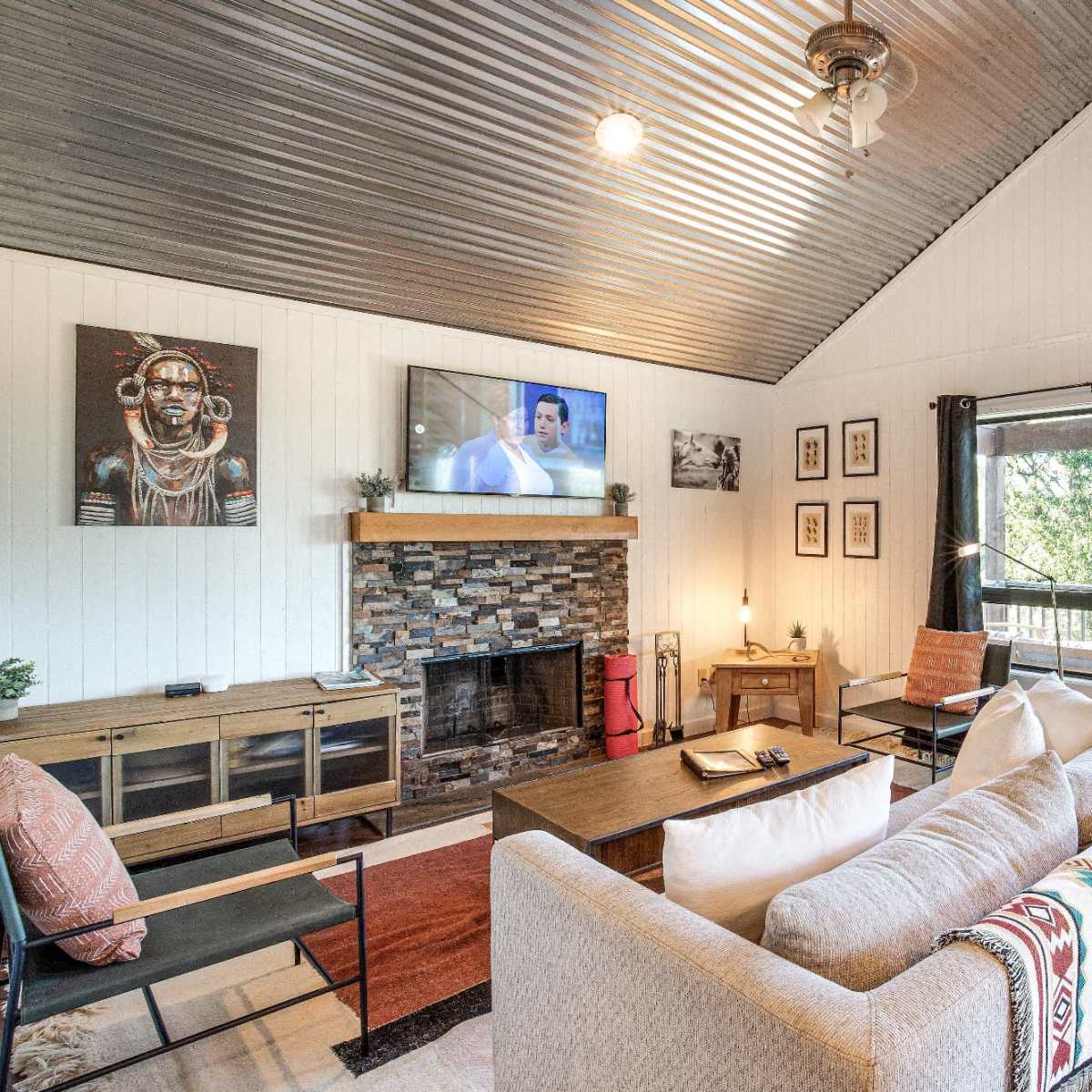 The living room features a cozy seating area with a beige sofa, a stone fireplace, a mounted television, and a bright orange front door.