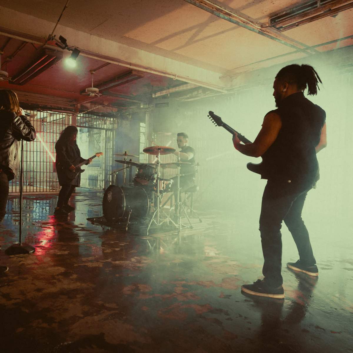 A band performs in a dimly lit, industrial space with fog and reflections on the floor.