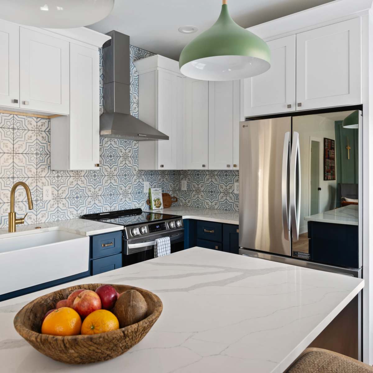 A modern kitchen with white cabinets, a blue island, and a bowl of fruit on the countertop.