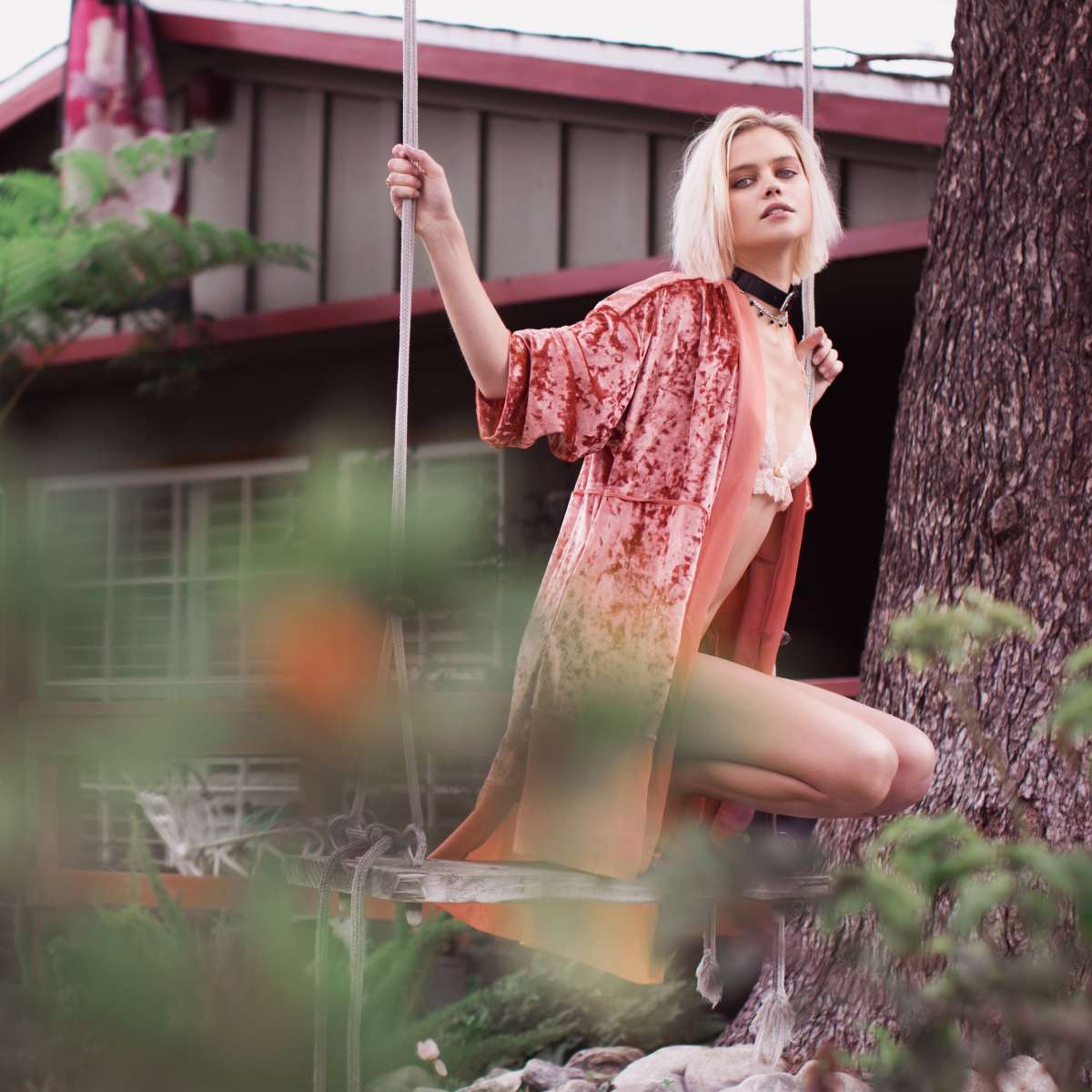 A person in a velvet cloak sits on a swing in a garden area near a house.