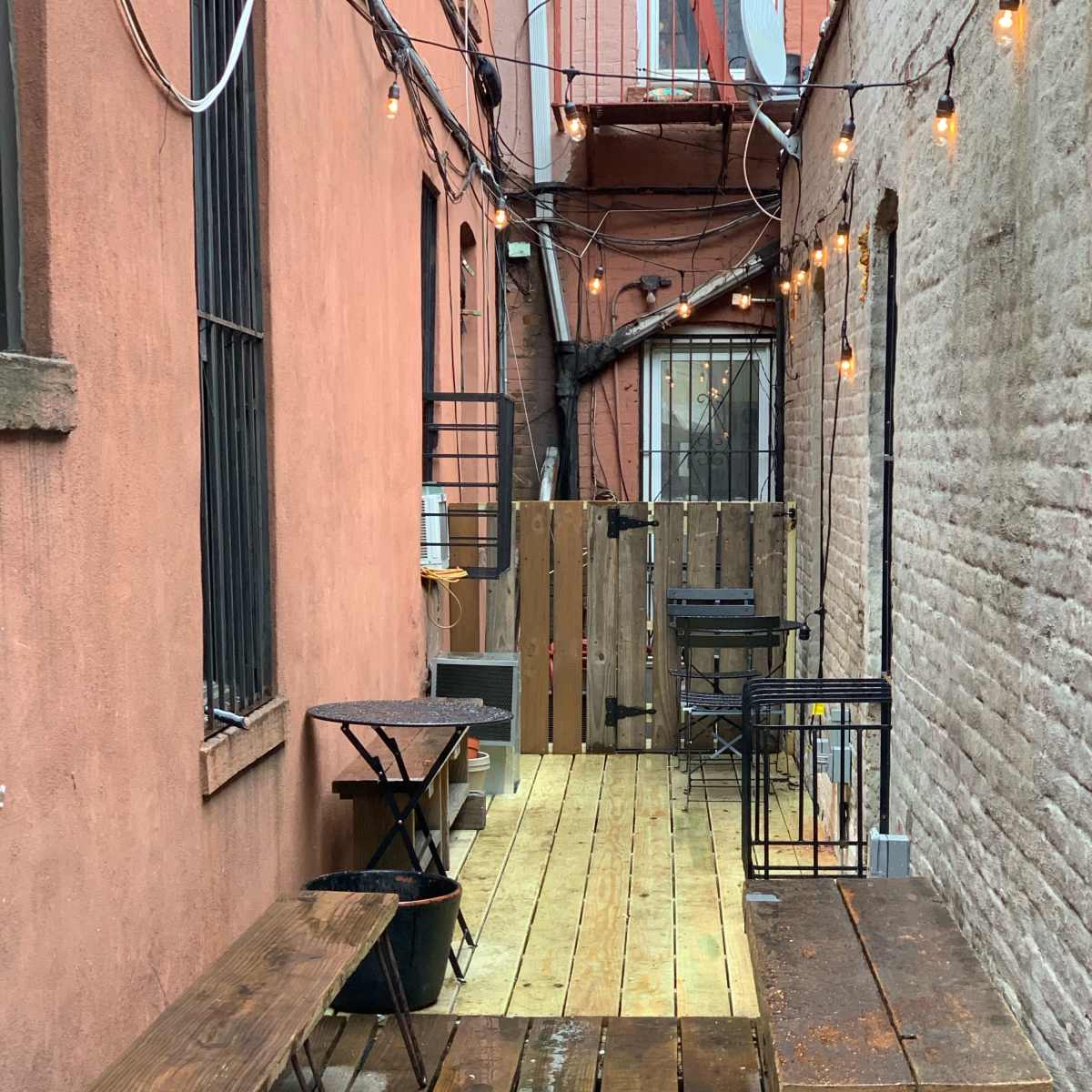 An alleyway with wooden flooring, two long benches, and strings of lights overhead.