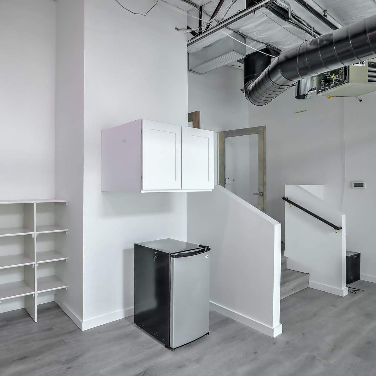 A small, modern room featuring a white shelving unit, a refrigerator, and a staircase.