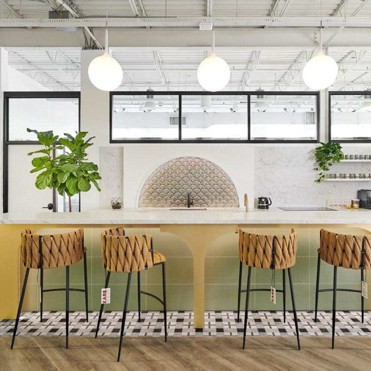 A modern kitchen with a large island bar featuring four high chairs and a decorative backsplash under pendant lights.