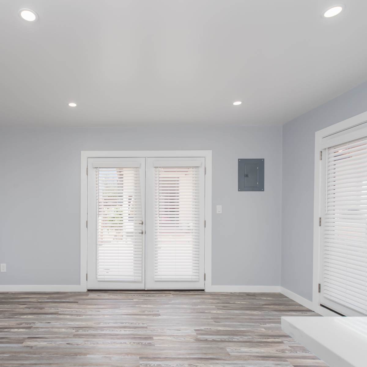 The room features light blue walls, wooden flooring, and two sets of white French doors with blinds.