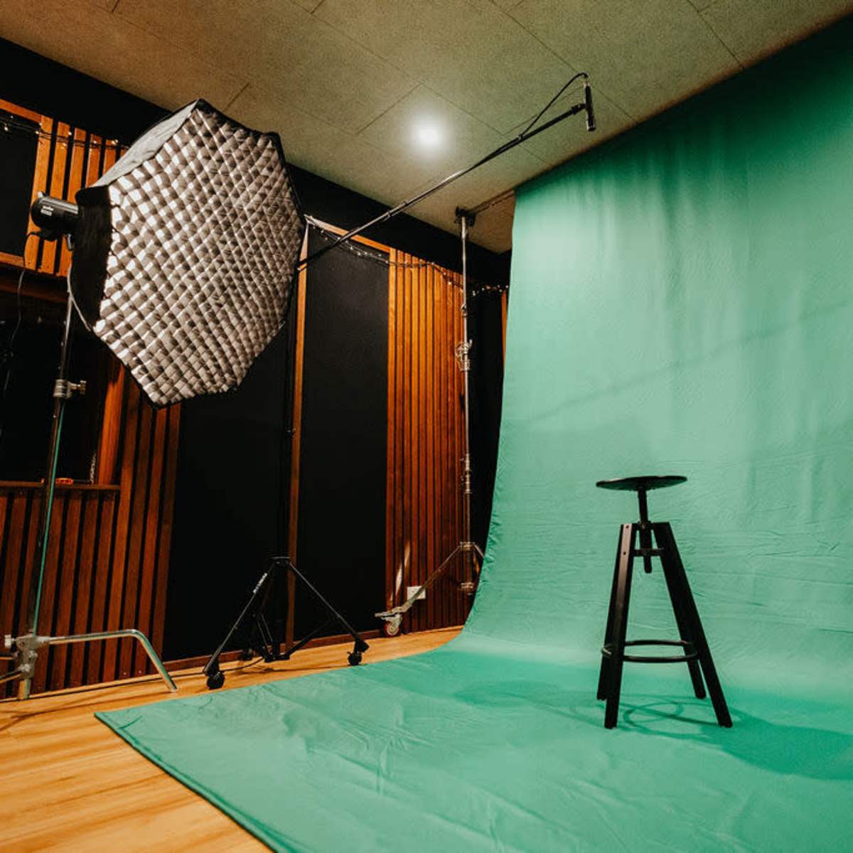 A photography studio setup featuring a green backdrop, a black stool in the center, and lighting equipment on the side.