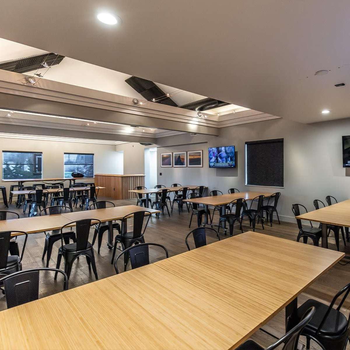 A spacious dining area with several tables and chairs arranged in rows, featuring a large television mounted on the wall.