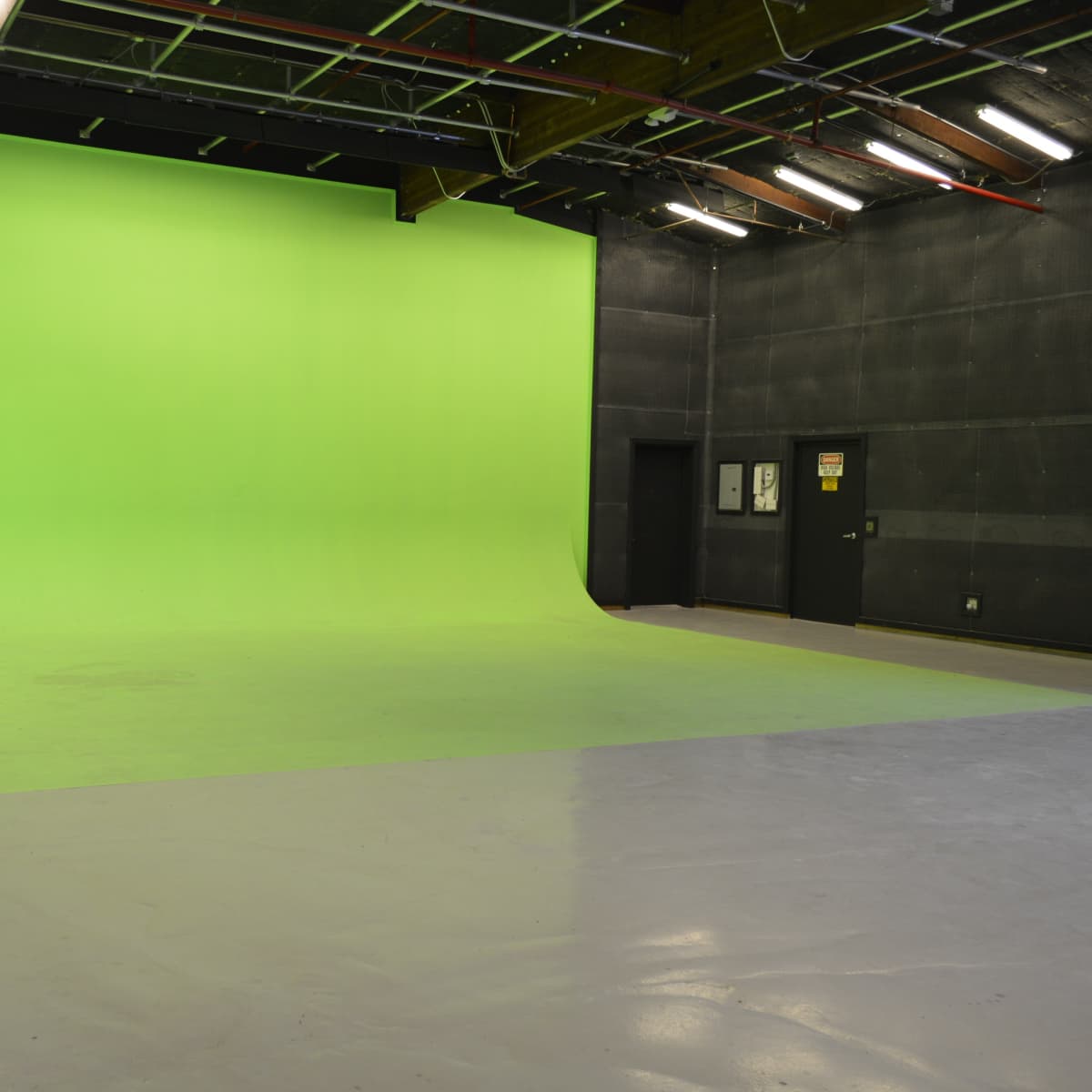 A spacious green screen studio with a curved backdrop and polished gray floor.