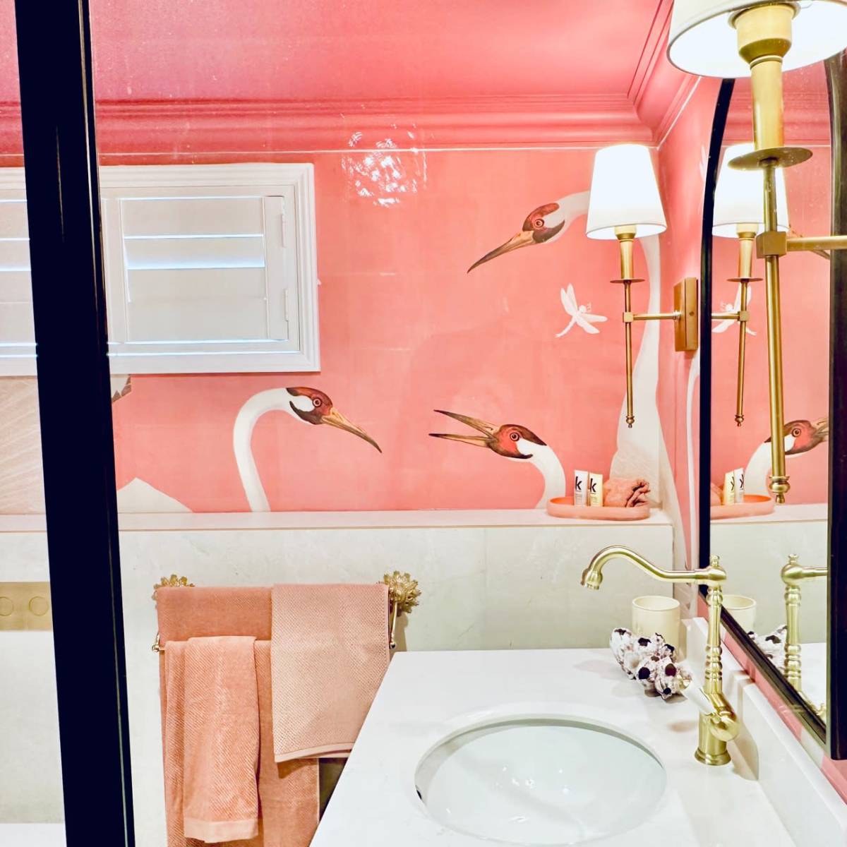 The bathroom features a pink wall with bird illustrations, a white sink, and gold fixtures.