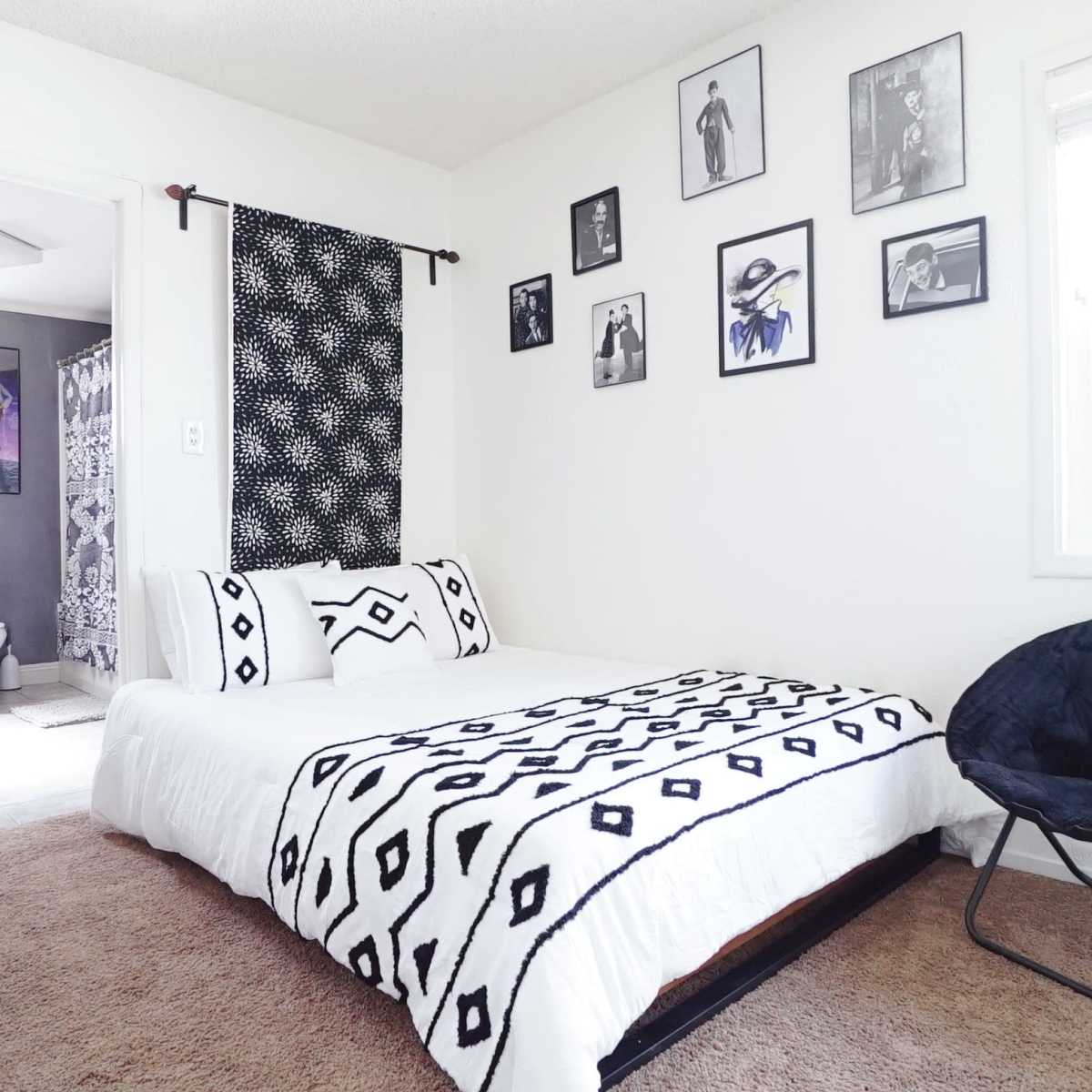 A bedroom with a bed covered in a black and white patterned blanket, a chair, and walls adorned with framed pictures.