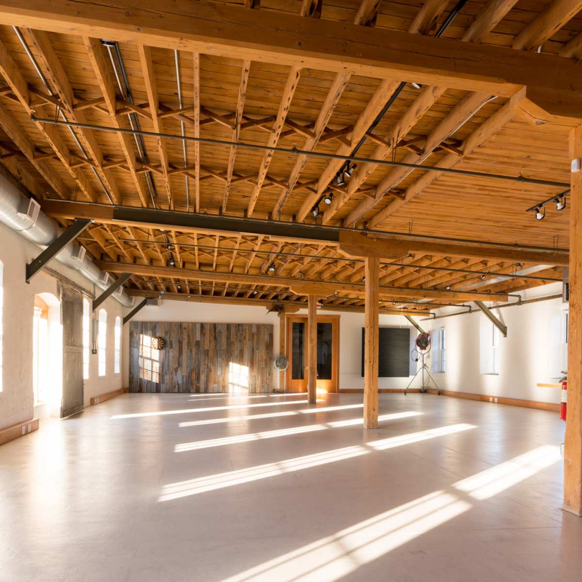 A spacious, well-lit interior with wooden beams and large windows, featuring concrete flooring and minimalistic decor.