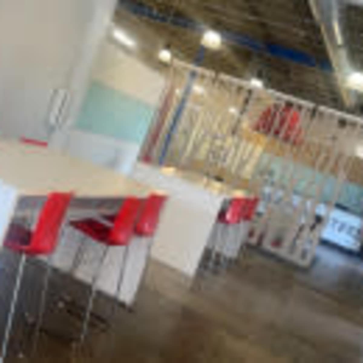 A modern workspace featuring several white tables paired with red chairs in a brightly lit, open environment.