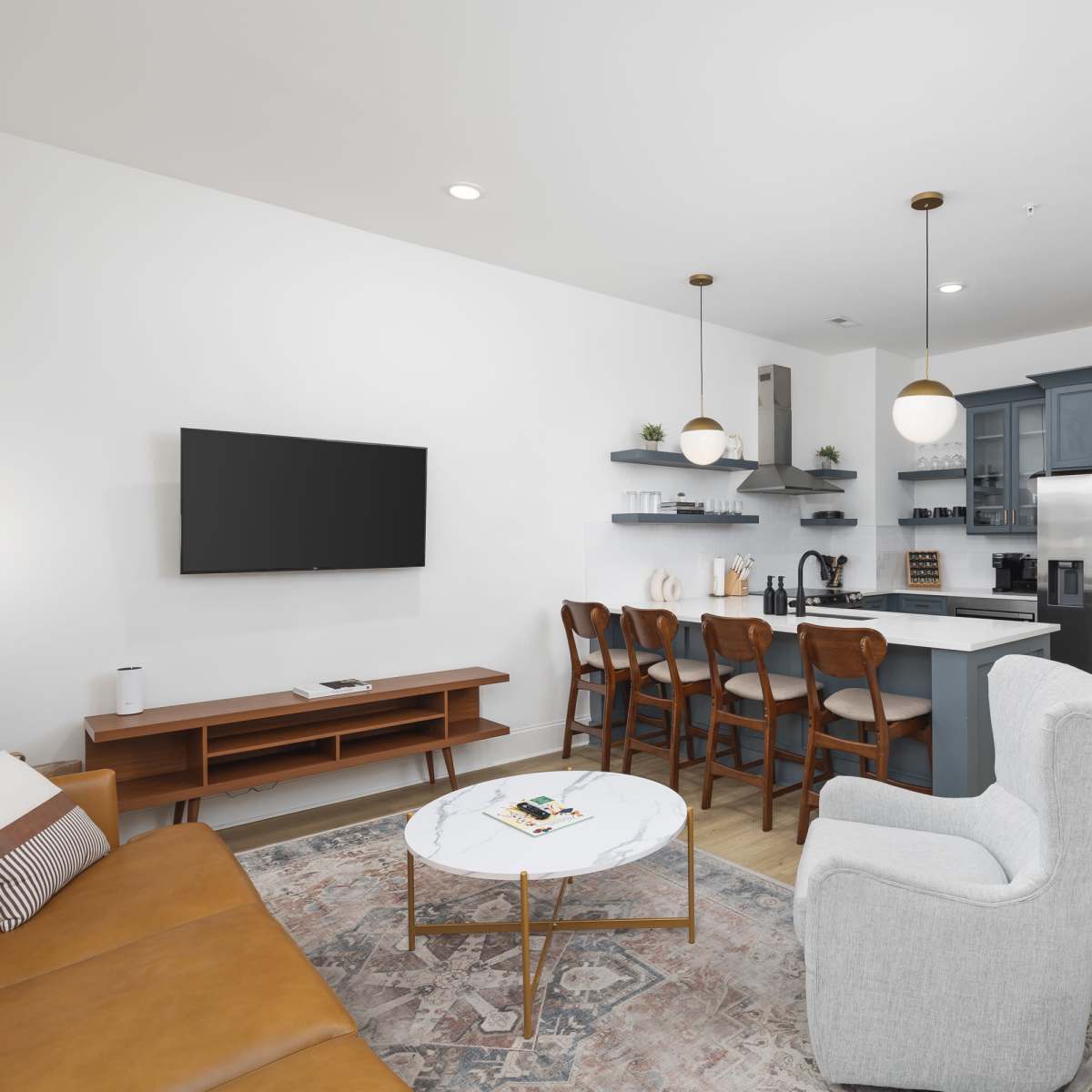 A modern living space featuring a leather sofa, a round coffee table, a dining area with wooden chairs, and a kitchen with stainless steel appliances.