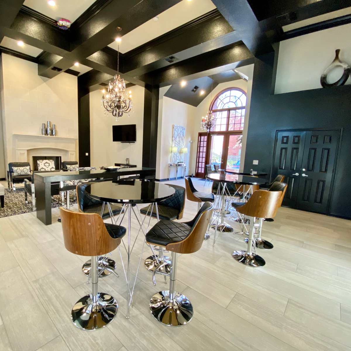 A modern lounge area with a central table surrounded by sleek bar stools, black and white decor, and a large arched window providing natural light.