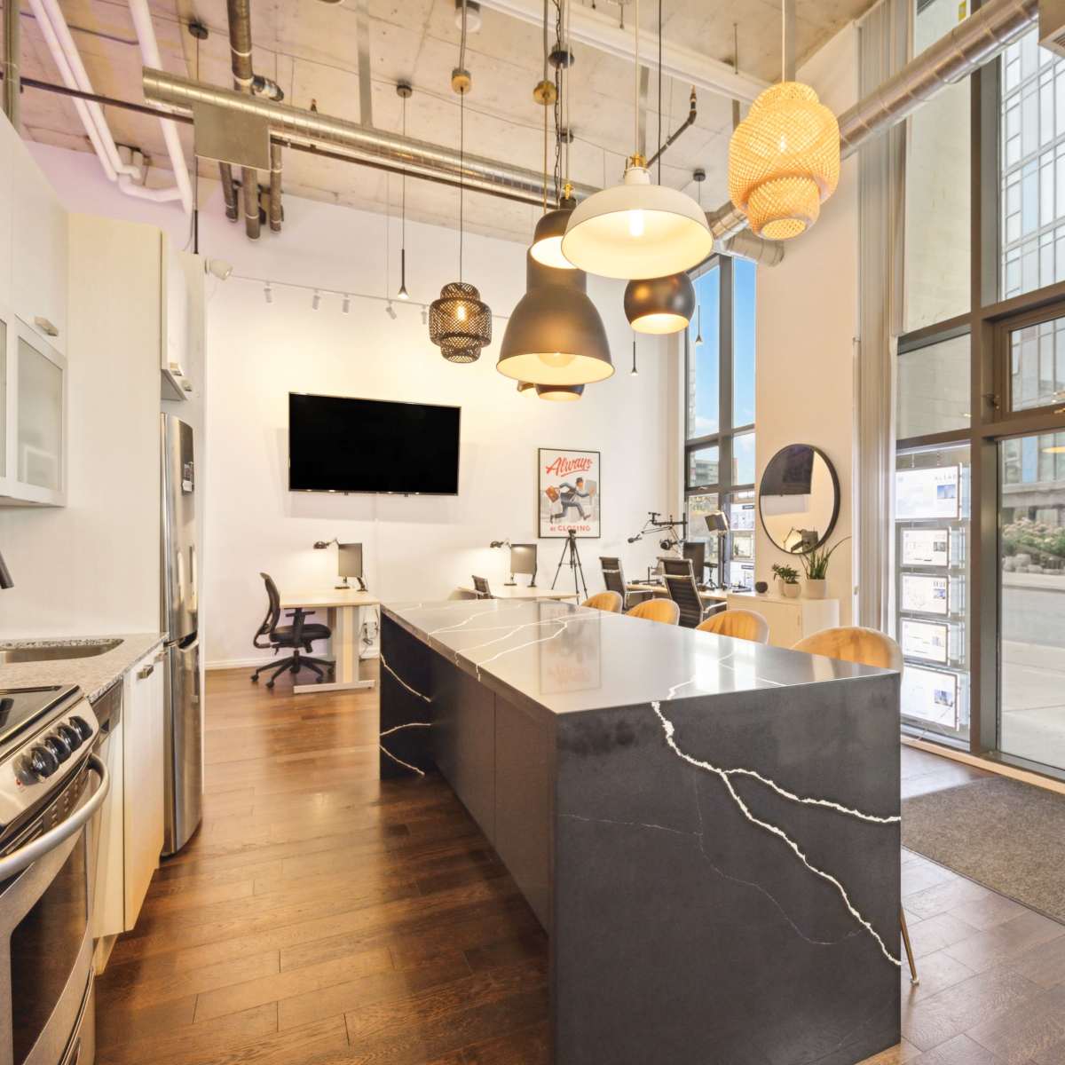 A modern kitchen with a large island, stainless steel appliances, and a seating area, set in a well-lit open space with large windows.