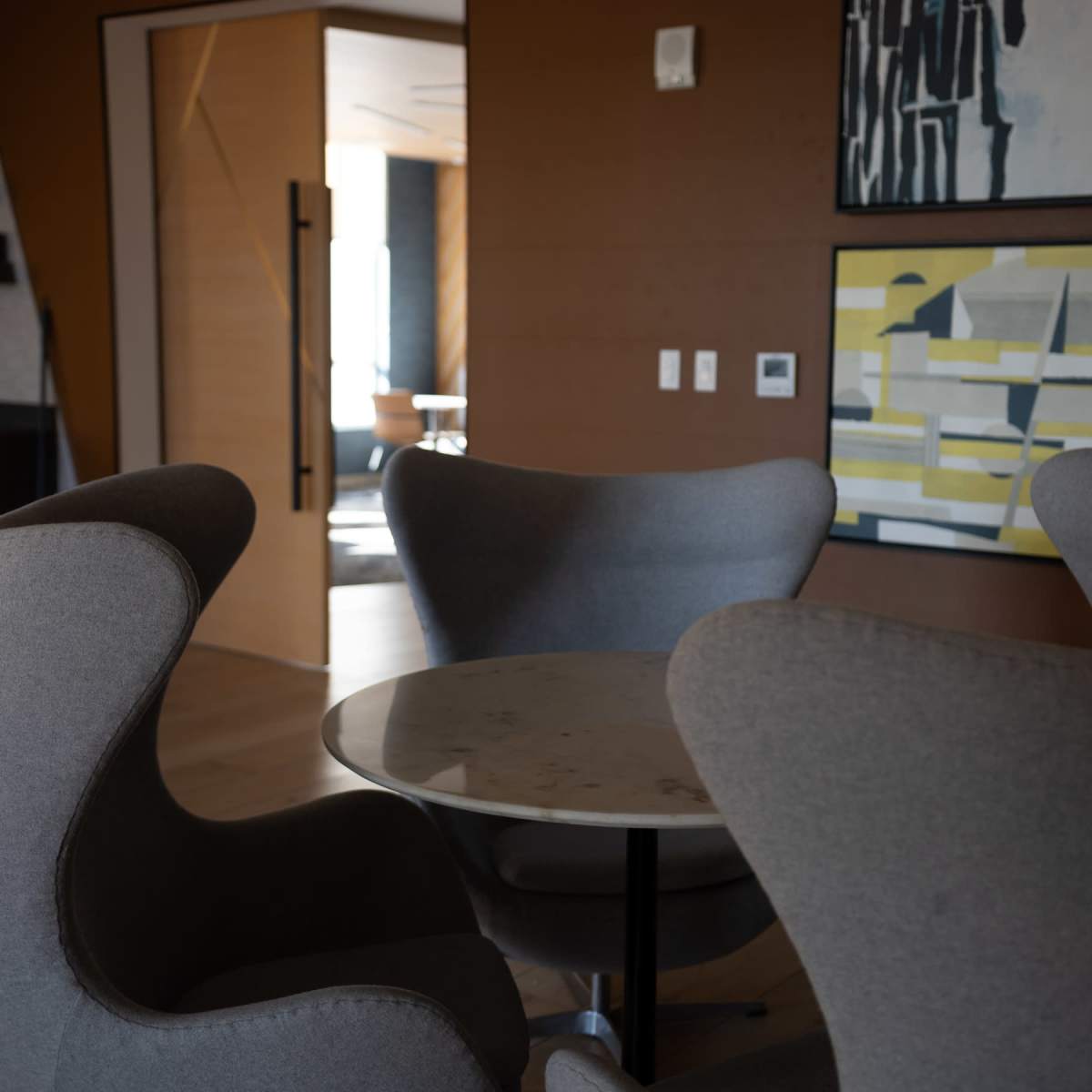 A modern interior space with four curved gray chairs surrounding a circular table and abstract art on the walls.