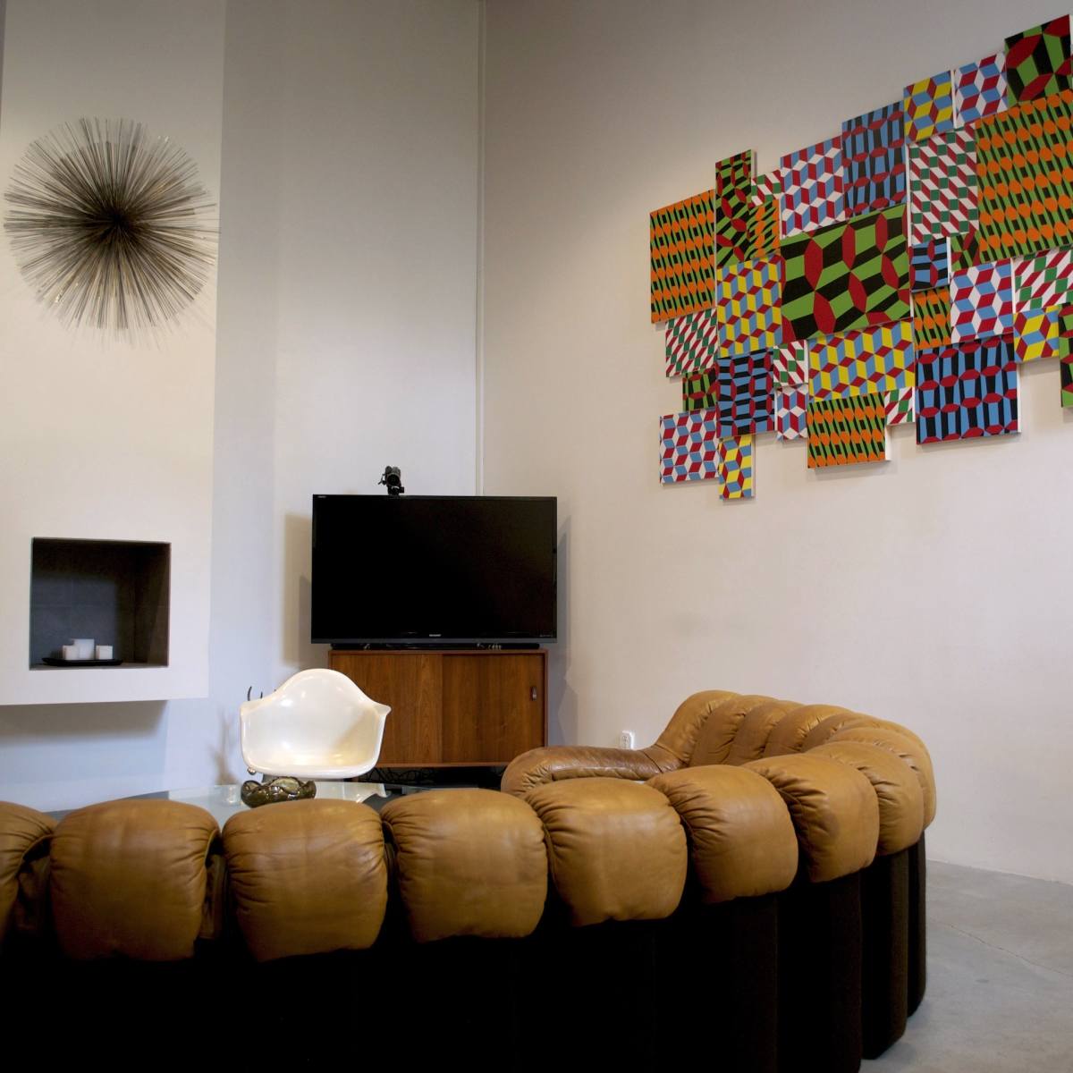 A modern living room with a circular brown leather sofa, a television, and a colorful geometric artwork on the wall.
