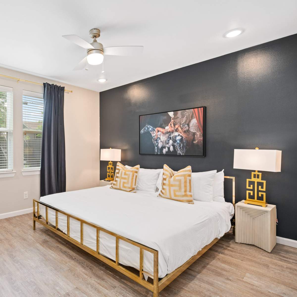A modern bedroom featuring a gold bed frame, two bedside lamps, a large wall art piece, and light-colored walls with dark curtains.