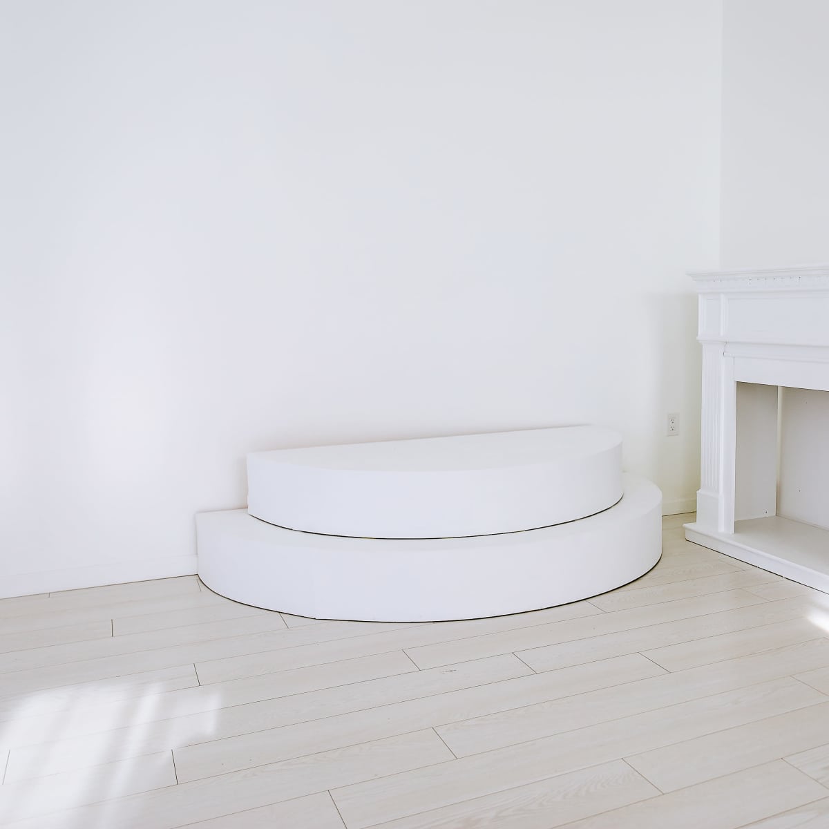 A minimalist room with a white curved bench and a white fireplace against a bright wall.