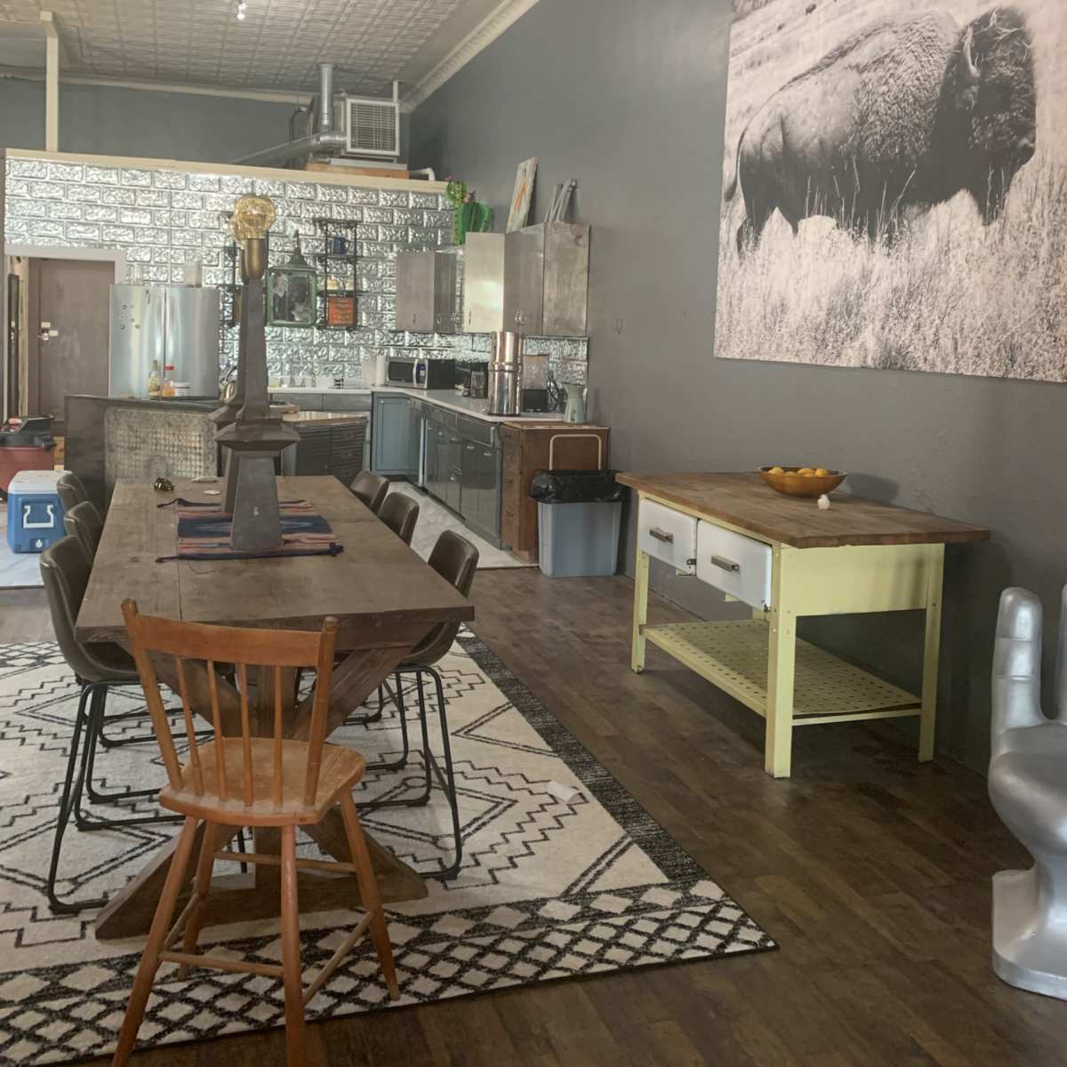 A modern kitchen and dining area featuring a large wooden table with chairs, stainless steel appliances, and a notable black-and-white photograph of a bison on the wall.