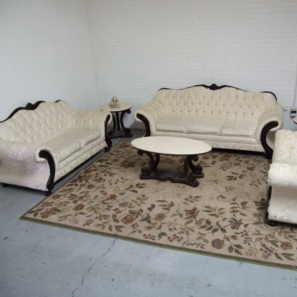 A sitting area with a white tufted sofa set arranged around a circular coffee table on a floral-patterned rug.