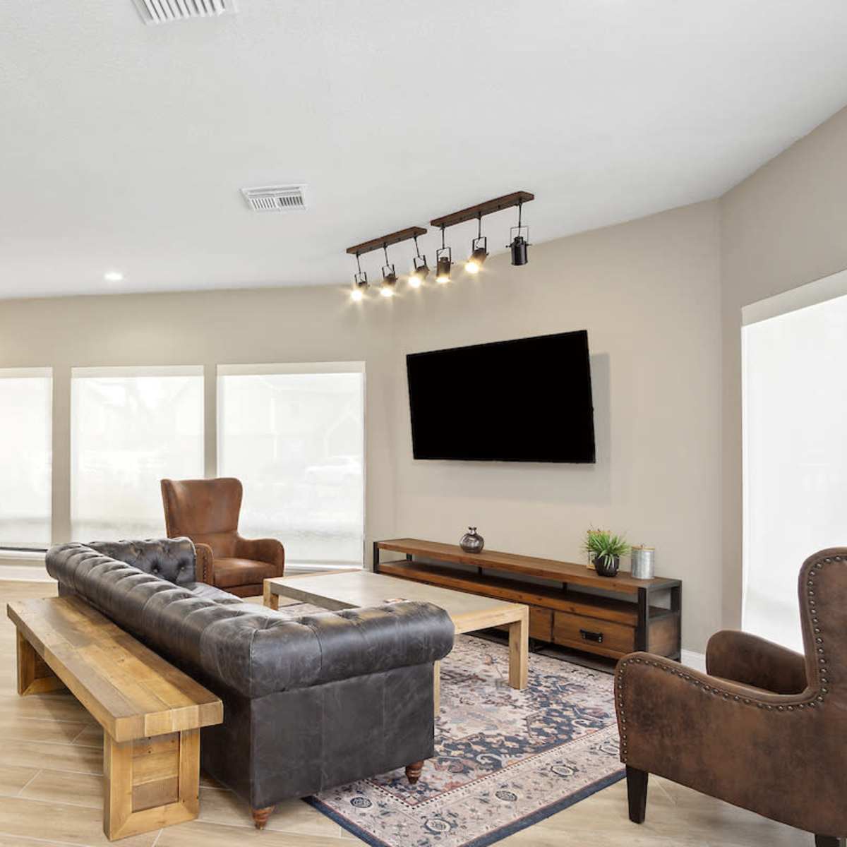 A spacious game room featuring a pool table, a leather sofa, armchairs, and a television mounted on the wall.