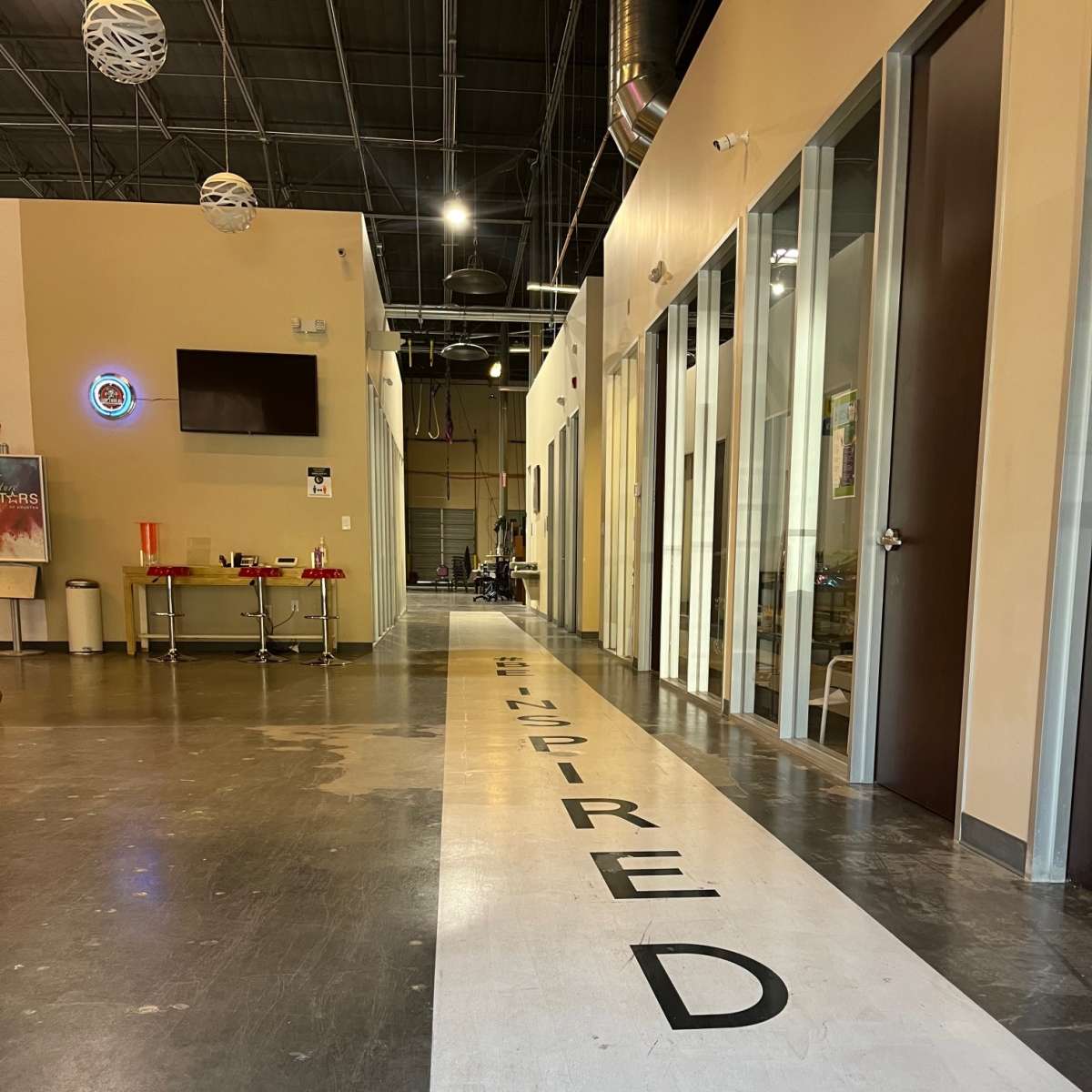 A corridor with the word "INSPIRED" prominently displayed on the floor, leading towards several doorways and a seating area.