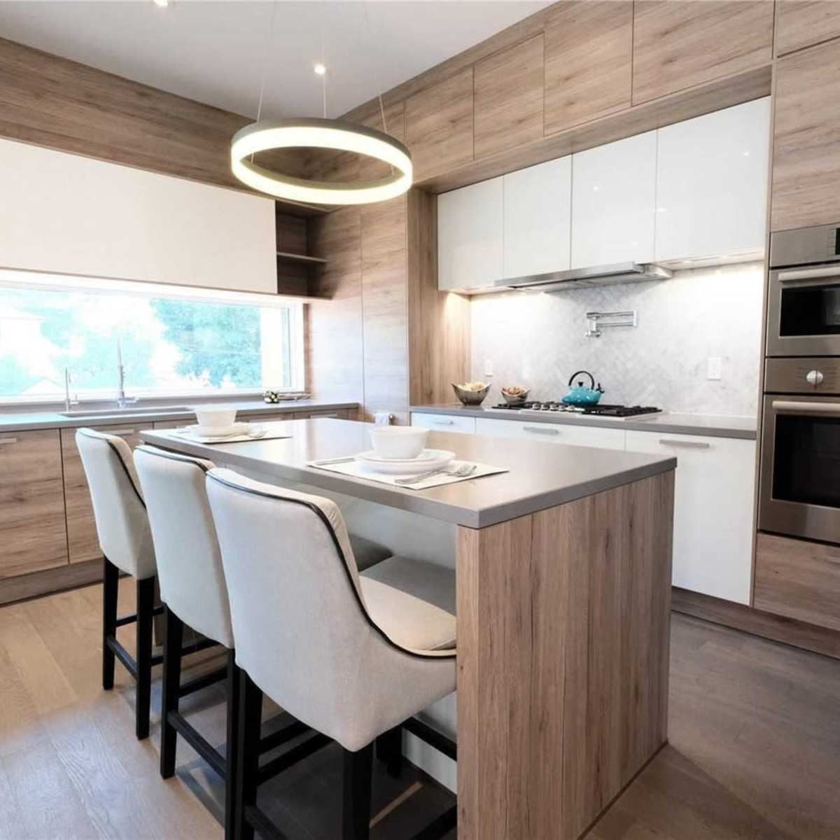 A modern kitchen features a central island with seating, sleek cabinetry, and built-in appliances against a backdrop of wood paneling.