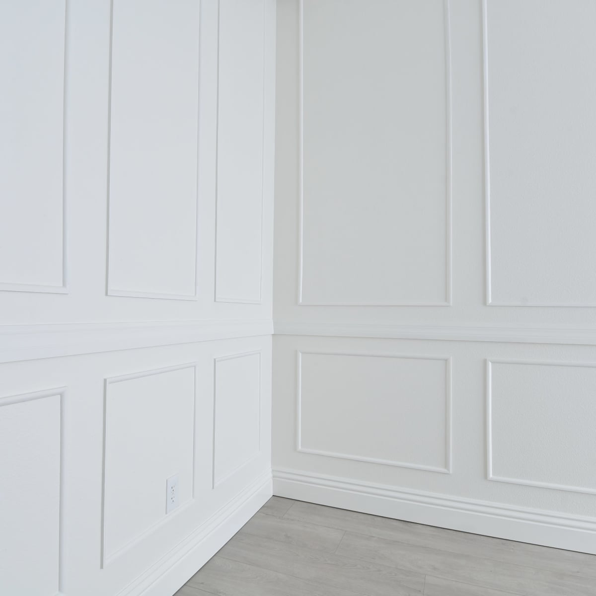 A corner of a room with white paneled walls and light gray flooring.