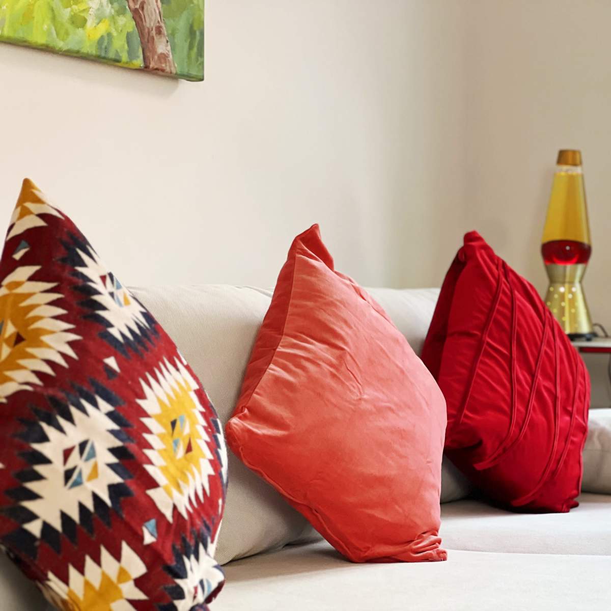 A couch with three decorative pillows sits in a well-lit room beside a small table with a lava lamp.