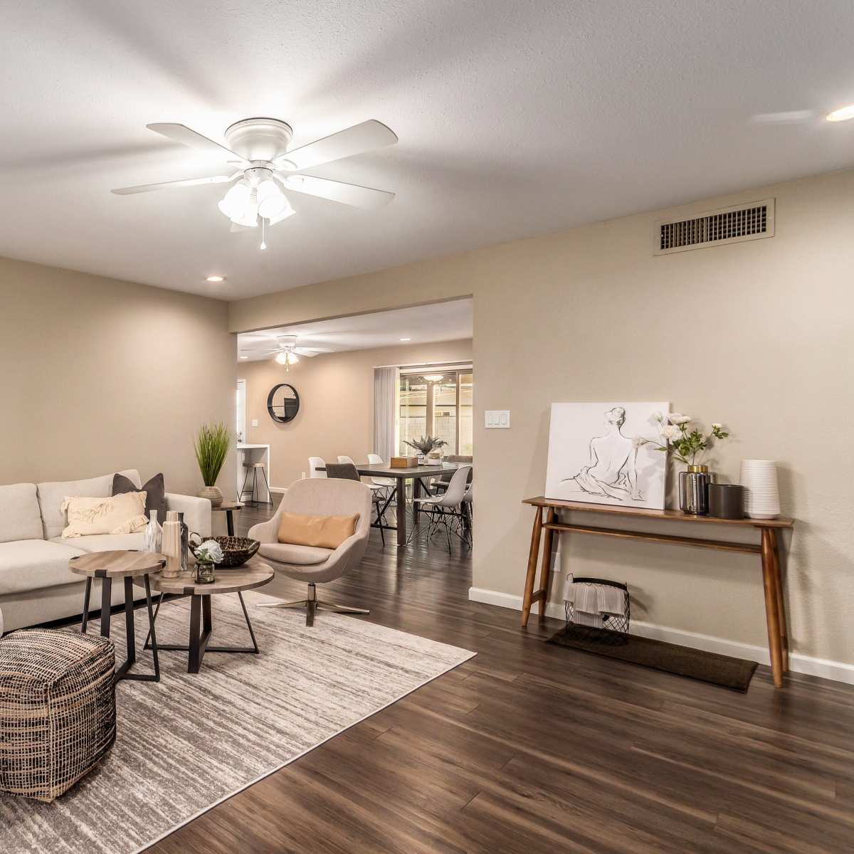 A modern living room featuring a light-colored sectional sofa, a round mirror on the wall, and a wooden side table with decorative items.