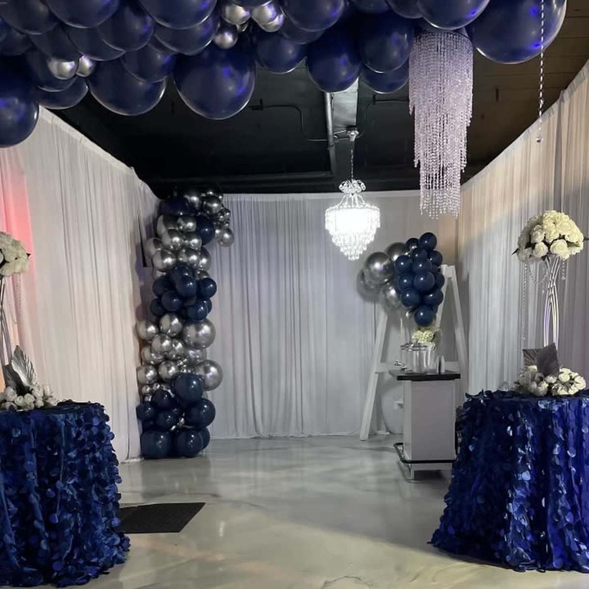 A decorated event space featuring a balloon arch, elegant tables with floral arrangements, and a chandelier overhead.