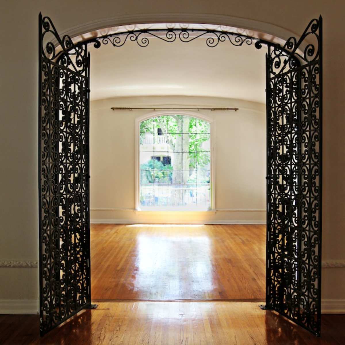 A pair of ornate wrought iron gates opening into a brightly lit room with a large window.