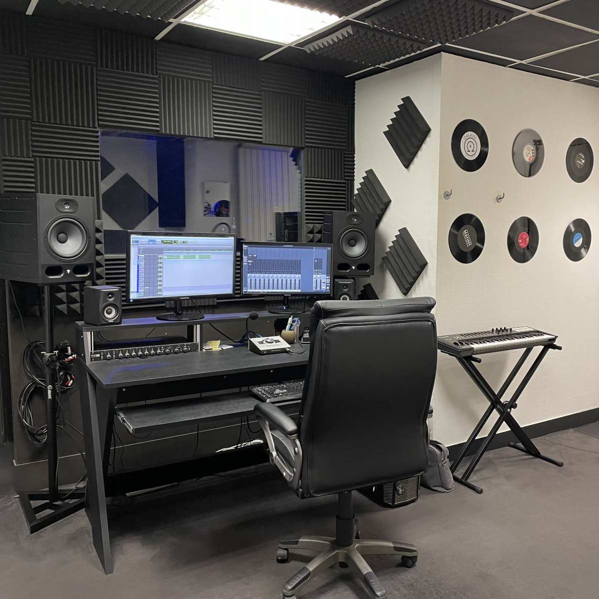 A music production studio featuring a computer workstation, audio speakers, and vinyl records displayed on the wall.