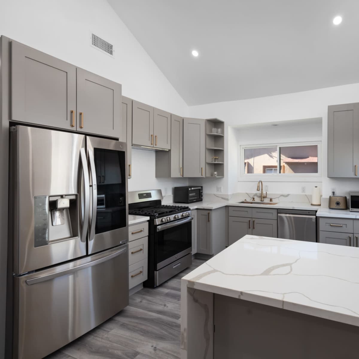 A modern kitchen with gray cabinets, stainless steel appliances, and a large island with a marble countertop.