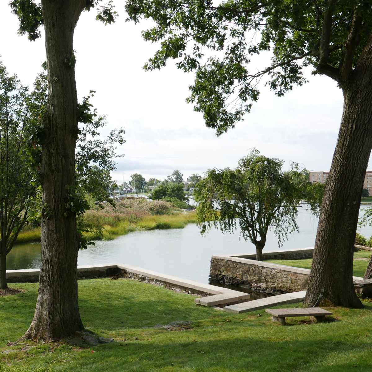 A tranquil landscape featuring a river bordered by trees and grassy areas, with stone pathways along the shore.