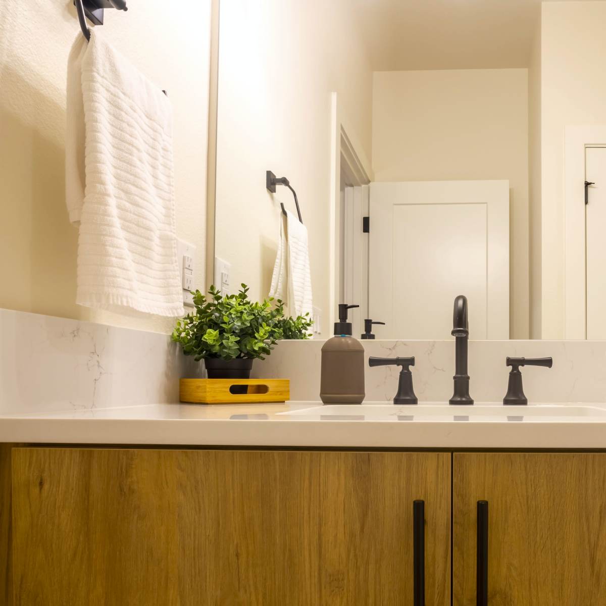 A bathroom countertop with neatly stacked white towels, a small potted plant, and modern faucet fixtures.