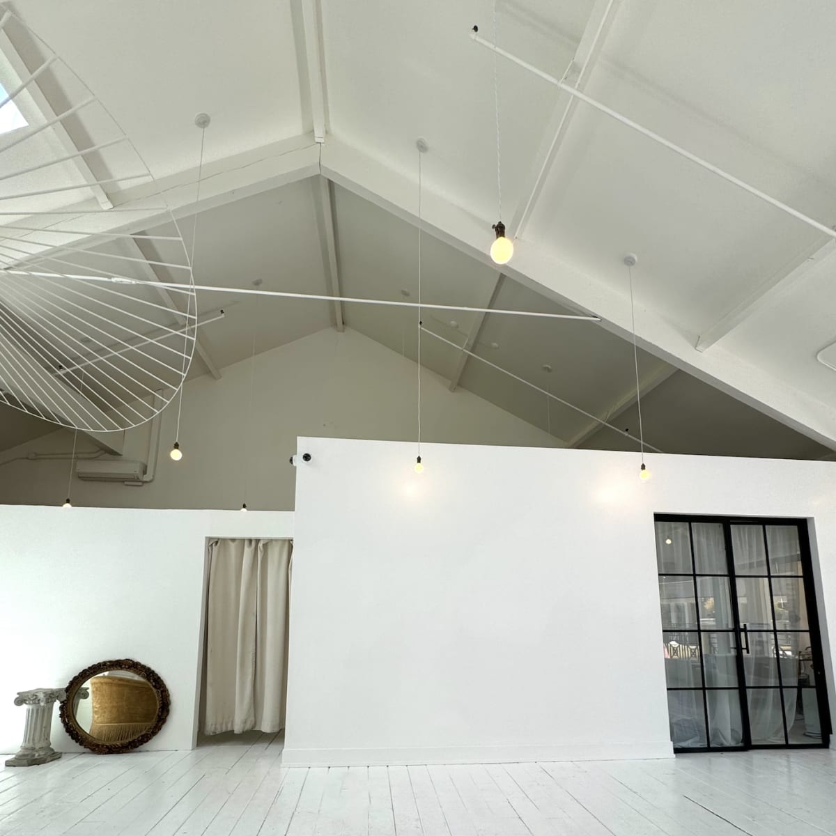 A spacious, bright interior with white walls, wooden flooring, and large windows.