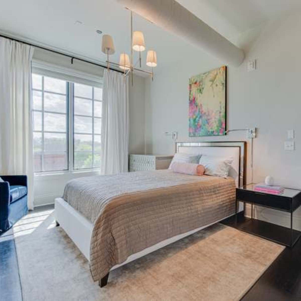 A modern bedroom with a bed, nightstand, and large window letting in natural light.