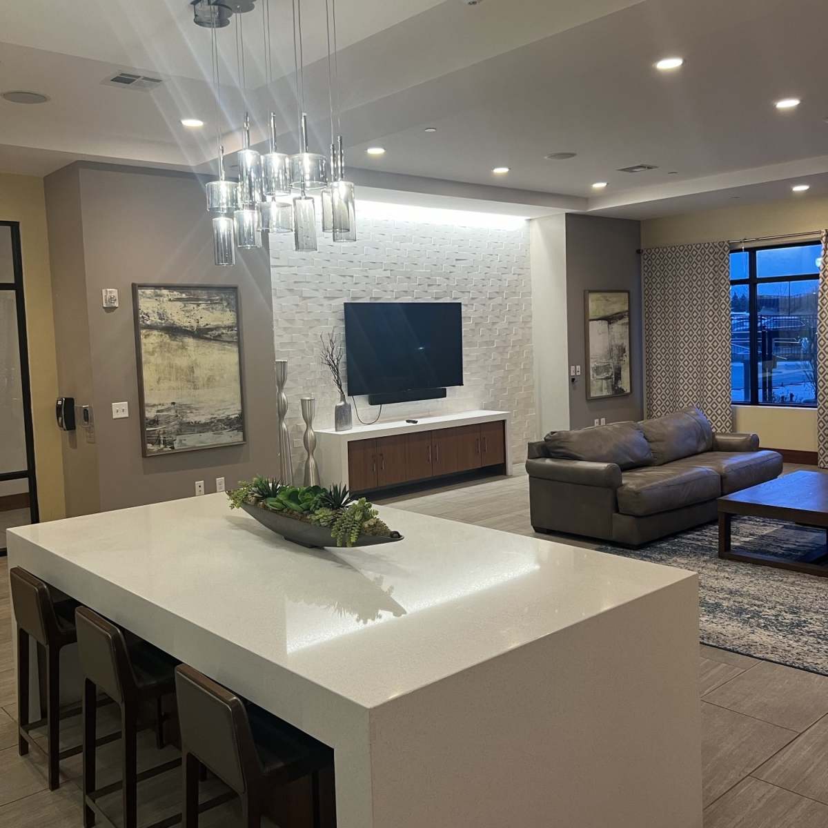 A modern living area with a kitchen island, a television mounted on the wall, and a comfortable sofa arranged around an area rug.