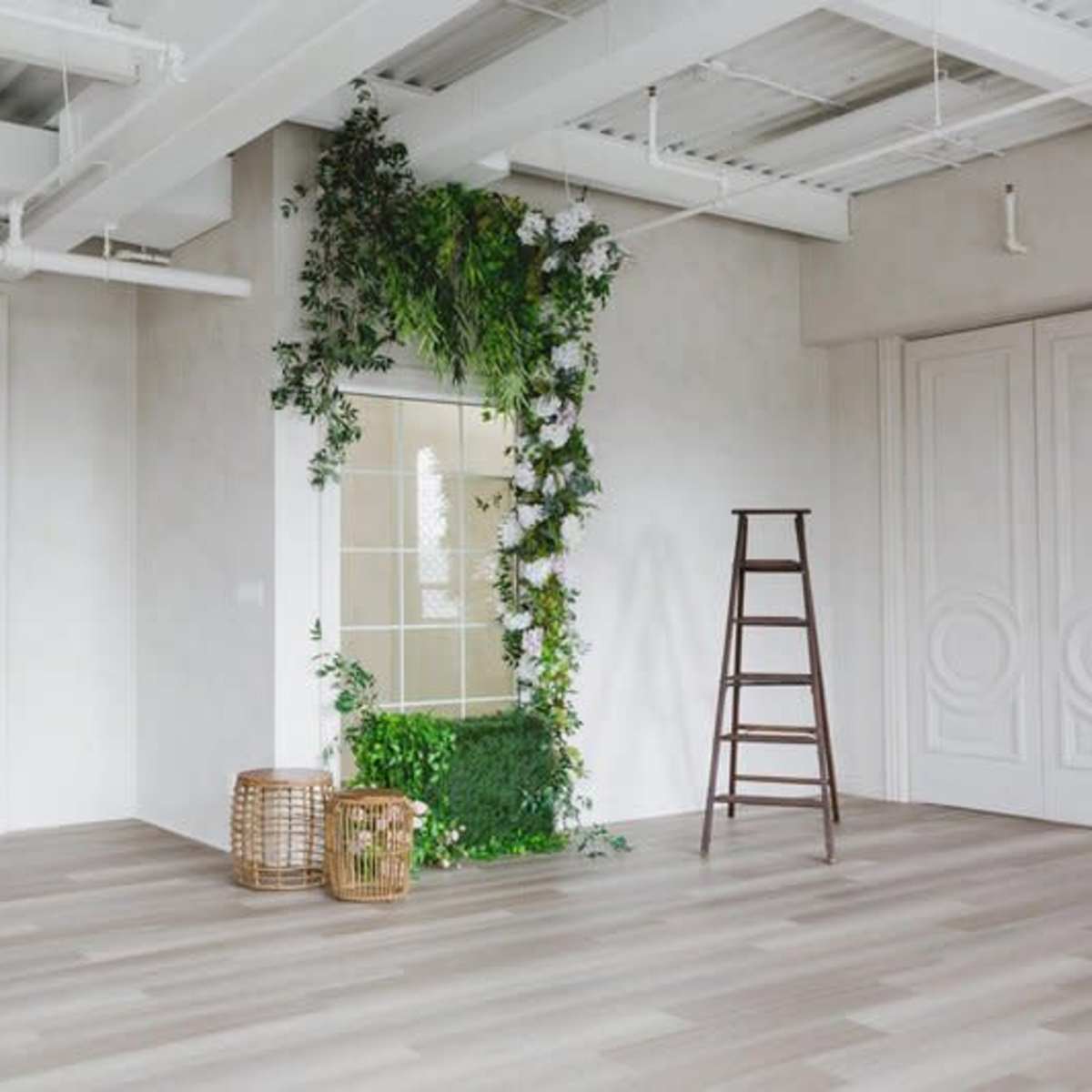 A spacious room featuring a decorative archway, a plant-filled wall, a wooden ladder, and two wicker baskets on the floor.