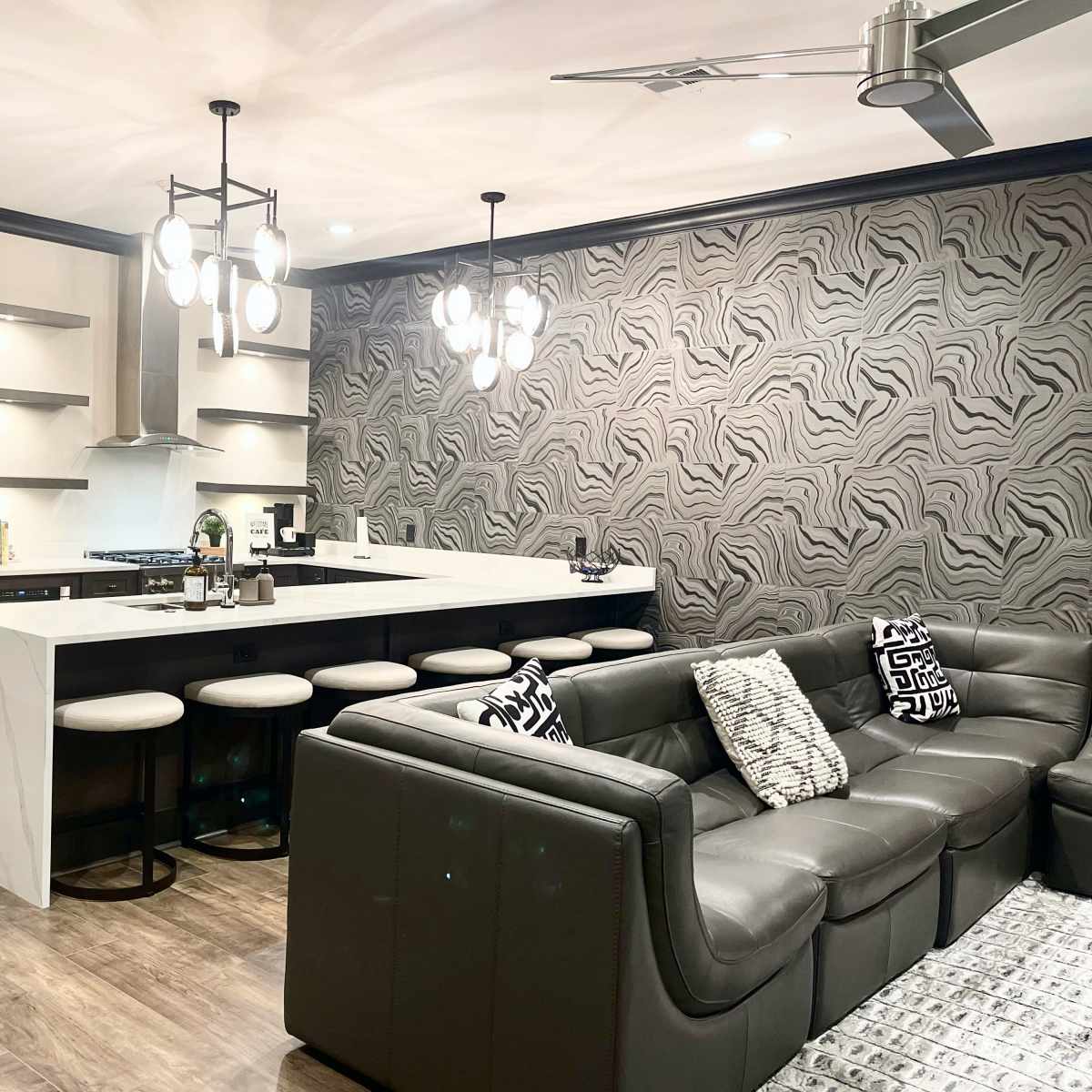A modern kitchen and living area featuring a sleek design with a large island, metallic appliances, and patterned wallpaper.