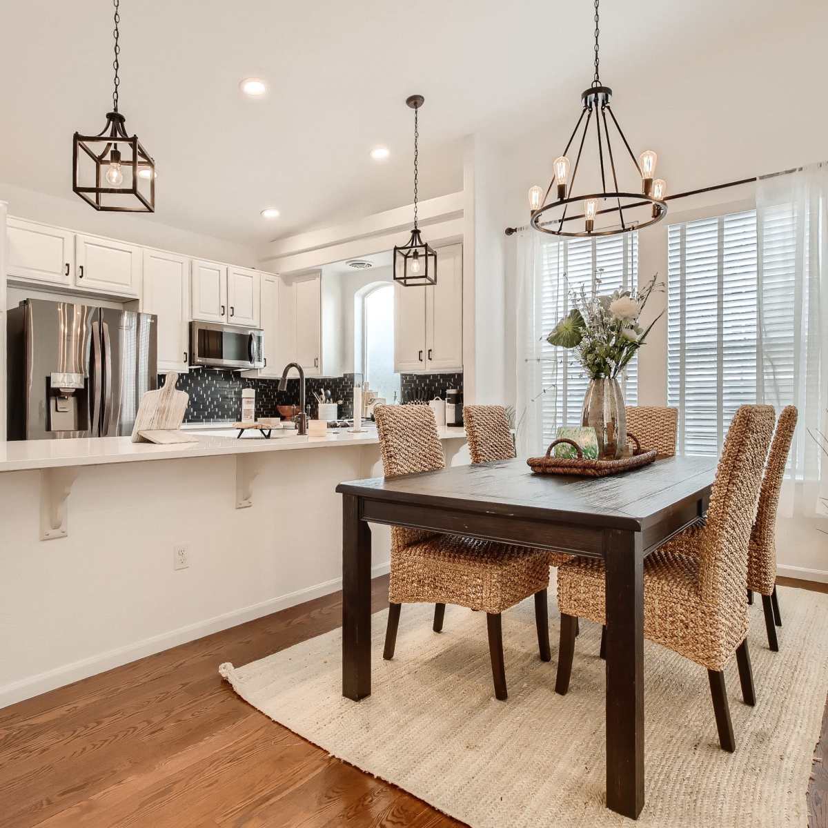 A dining area features a dark wooden table surrounded by woven chairs, with a kitchen visible in the background.