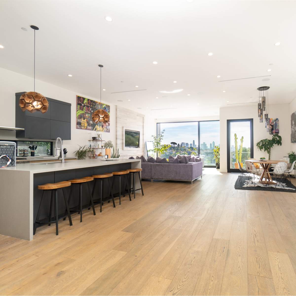 A modern open-concept living space featuring a kitchen island, dining area, and lounge with large windows overlooking a city skyline.