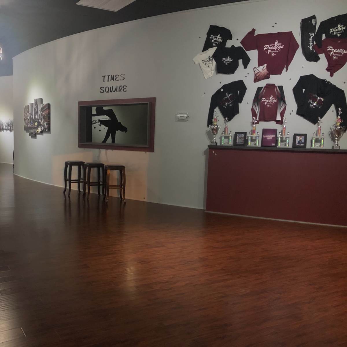 The interior of a dance studio features a curved wall displaying shirts, a TV screen, and a row of trophies along with a seating area.
